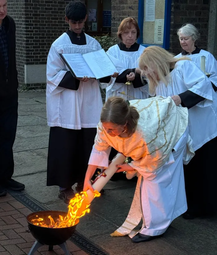 A priest lights the Paschal candle from the new fire as servers look on
