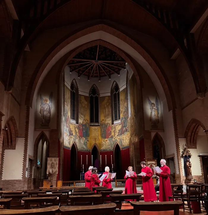 Choir in red robes sings before the high altar beneath a large wall mural