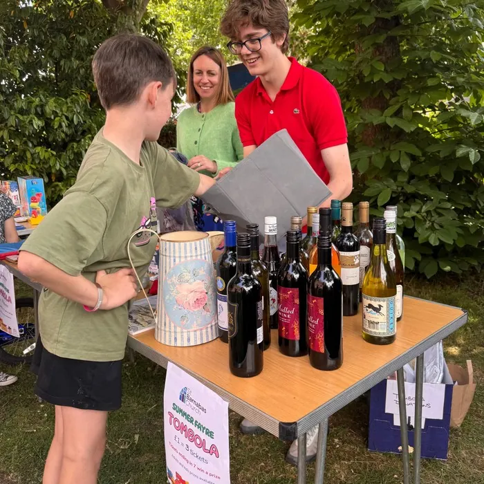 Volunteers and a young visitor at a tombola stall lined with bottles